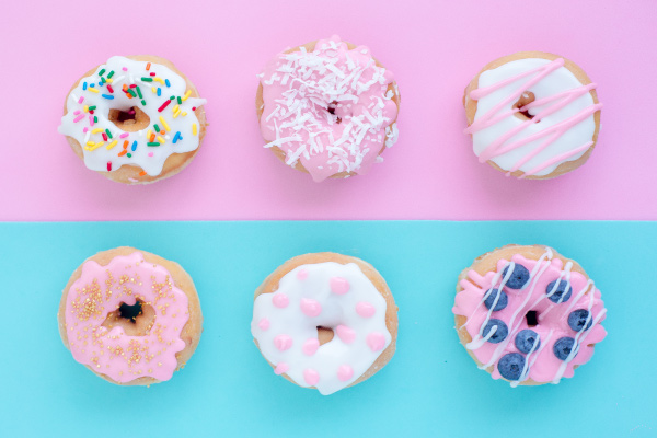 Aerial view of six donuts on a half pink, half blue counter with pink and white icing, sprinkles, and shredded coconut