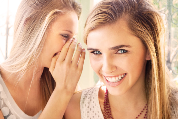 young women with veneers whispering and smiling