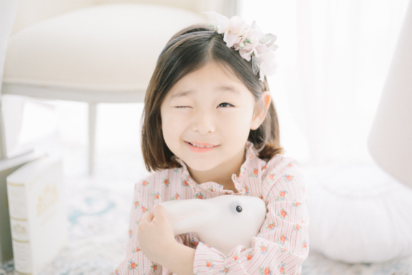 Dark-haired girl wearing a floral dress winks as she hugs a bunny stuffed animal to stay calm about visiting the dentist