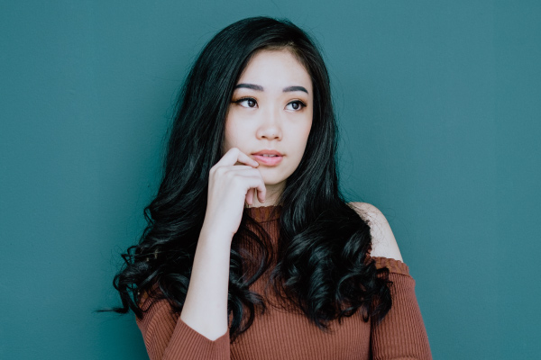 Dark-haired woman wearing a copper sweater puts a hand on her chin wondering about the oral cancer screen at the dentist